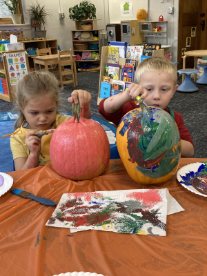 Two children are painting real pumpkins
